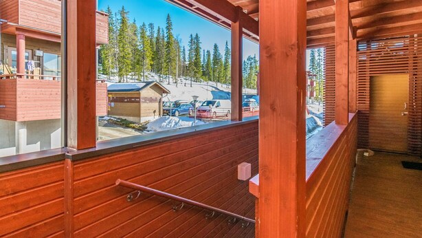 A wooden balcony with a metal railing overlooking a parking area and a building with a sloped roof. - Länsirinne e 20 by Interhome (Kuusamo)