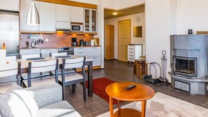 A modern kitchen with white cabinets, a microwave, and a coffee maker. There is a dining area with a table and chairs, and a fireplace in the living room. - Länsirinne e 20 by Interhome (Kuusamo)