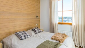 A bedroom with a wooden panel wall, a bed with two pillows, a blanket, and a window with curtains. - Länsirinne e 20 by Interhome (Kuusamo)