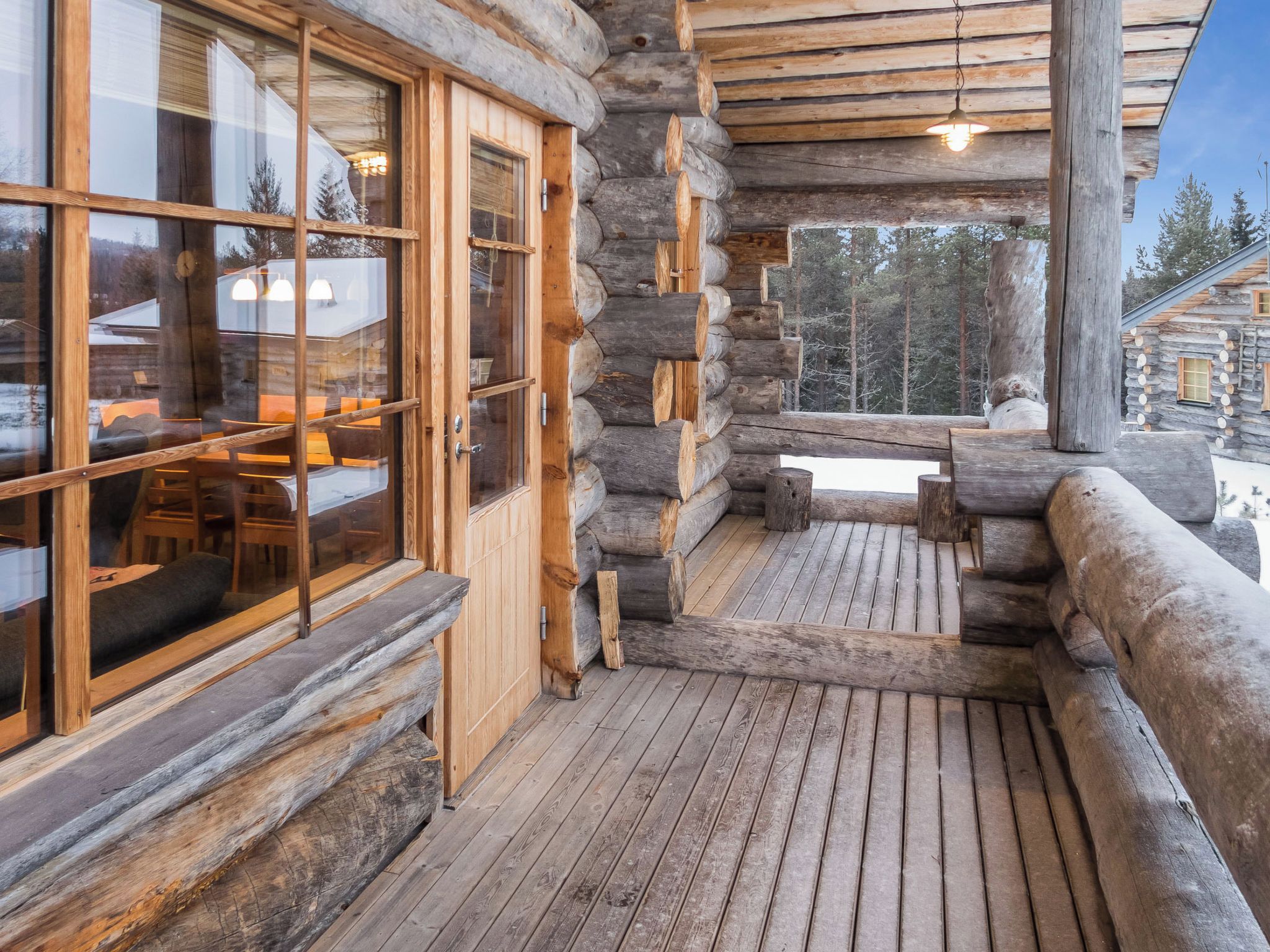 A log cabin with a wooden deck, large windows, and a view of the surrounding forest.