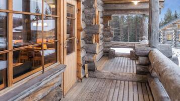A log cabin with a wooden deck, large windows, and a view of the surrounding forest.