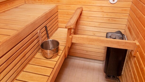 A wooden sauna with benches, a metal basin, and a towel rack. - Alppitalo punatähti 7 as 2 by Interhome (Nilsiä)