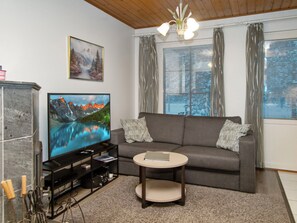 A living room with a flat-screen TV, a gray sofa, a small round coffee table, and a bookshelf. - Alppitalo punatähti 7 as 2 by Interhome (Nilsiä)