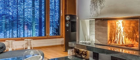 A modern living room with a fireplace, large windows, and a view of a snowy forest.