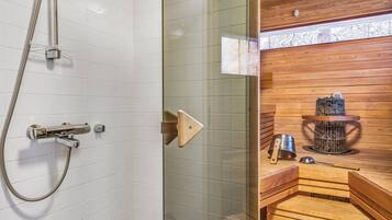 A modern bathroom with a glass shower enclosure, a wooden sauna area, and a visible sauna heater.
