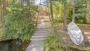 A wooden pathway leading to a cabin in a forested area with a boat nearby.