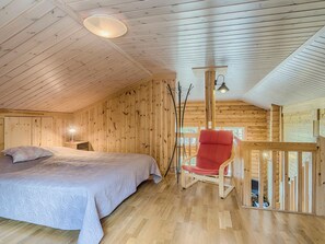 Et hyggeligt træværelse med seng, rød stol og et lille bord med lampe.