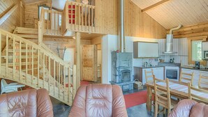 A cozy cabin interior with a wooden staircase, a fireplace, a kitchen area, and leather seating.