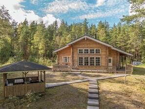 A log cabin with a porch, a covered picnic area, and a wooden deck leading to the entrance.