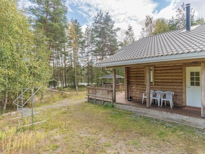 Une cabane en bois avec une véranda, deux chaises en plastique blanc et un étagère en métal.