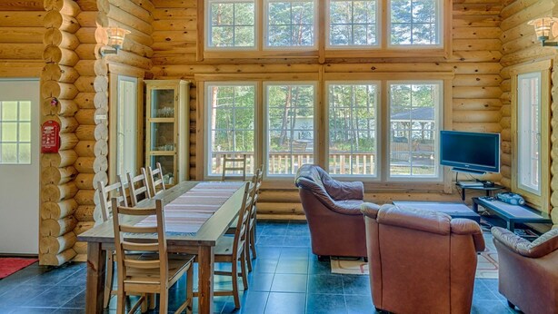 A log cabin interior with a dining area, seating, and a television.