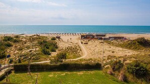 Un resort frente al mar con un sendero de arena que lleva a la playa, sombrillas y cabañas.