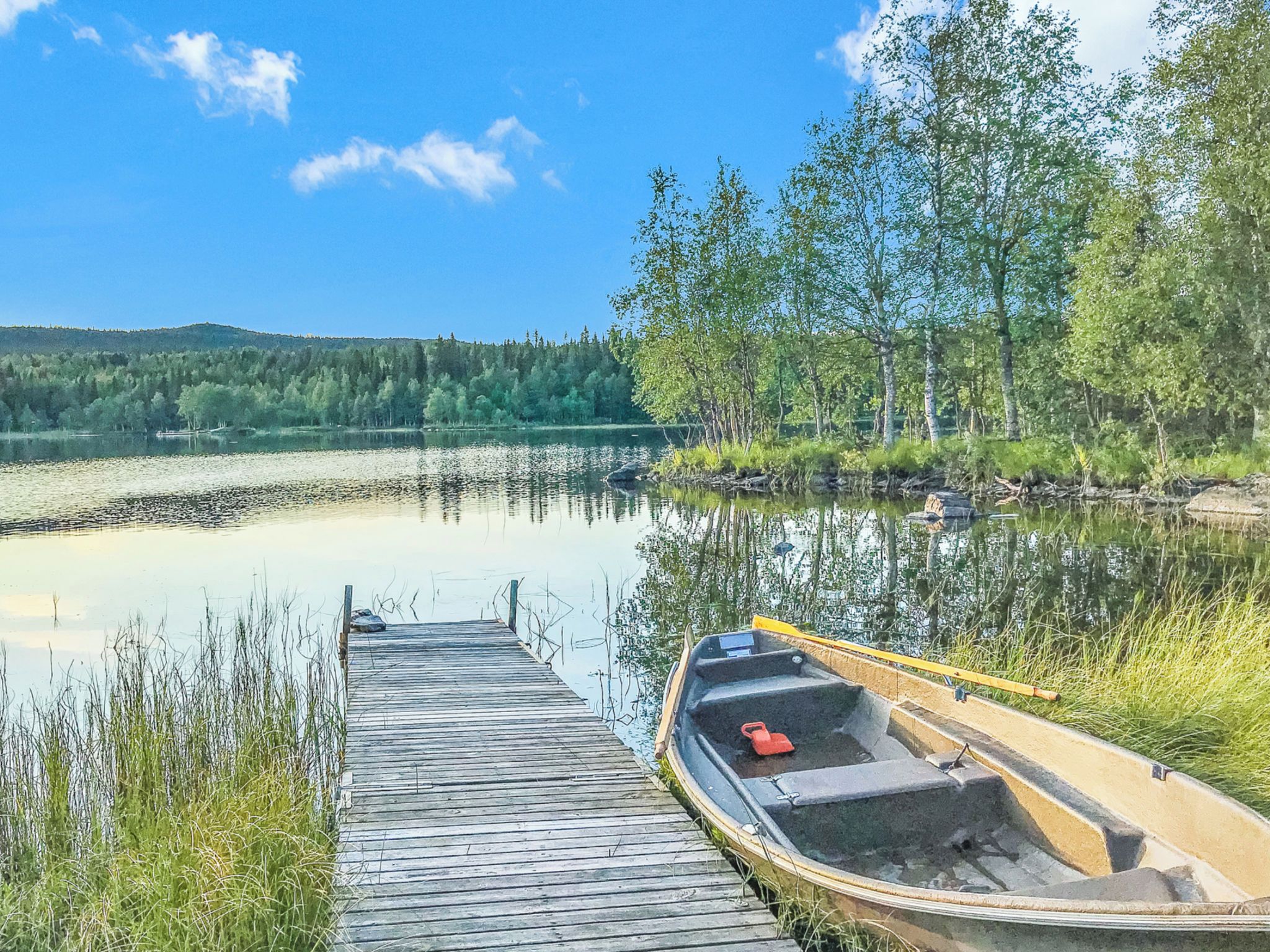 A wooden dock leading to a calm lake with a boat moored at the end.