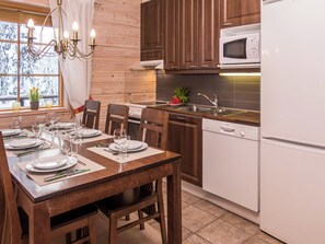 A modern kitchen with wooden cabinets, a white Bosch dishwasher, and a dining area set for six with a chandelier.