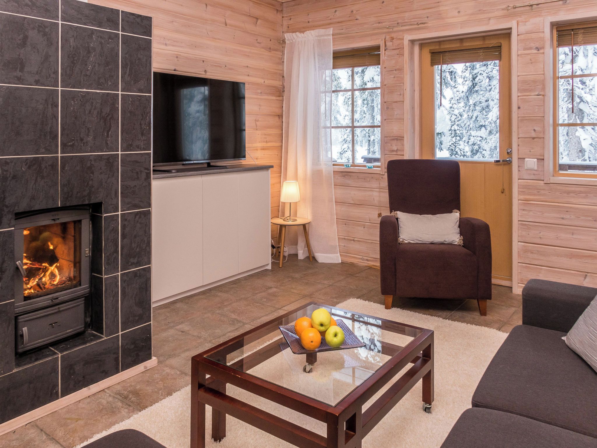 Una sala de estar acogedora con chimenea, un televisor de pantalla plana, un sillón cómodo y una mesa de centro con fruta.