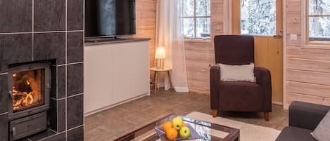 Ein gemütliches Wohnzimmer mit Kamin, einem Flachbildfernseher, einem bequemen Sessel und einem Couchtisch mit Früchten.