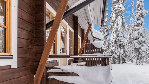 A wooden cabin with a covered porch and a snow-covered landscape.