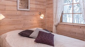 A cozy wooden cabin room with a bed, a wall-mounted lamp, and a window with curtains.