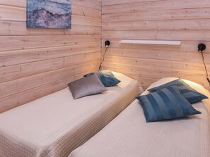 A room with two beds, each with a pillow and a headboard. There is a painting on the wall above the beds.