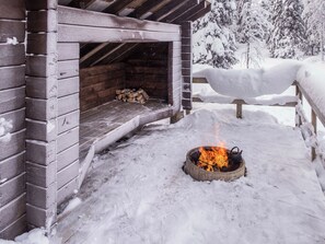 A wooden cabin with a fireplace, snow-covered surroundings, and a wooden fence.