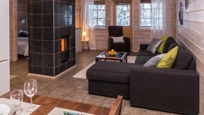A cozy cabin interior with a fireplace, a sofa, a dining area, and a view of snowy trees through the windows.