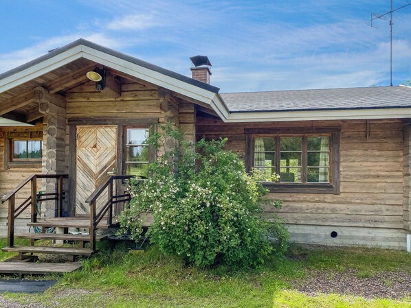 Een blokhut met een houten trap naar een deur, een klein terras en een raam met uitzicht op de omliggende begroeiing.