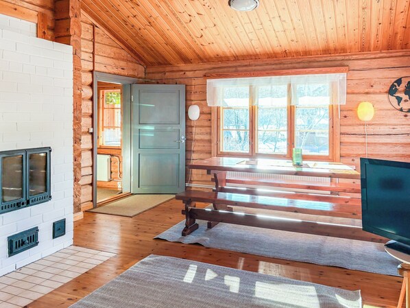 En stuga byggd av timmer med en öppen spis, trägolv, ett matbord och en tv.