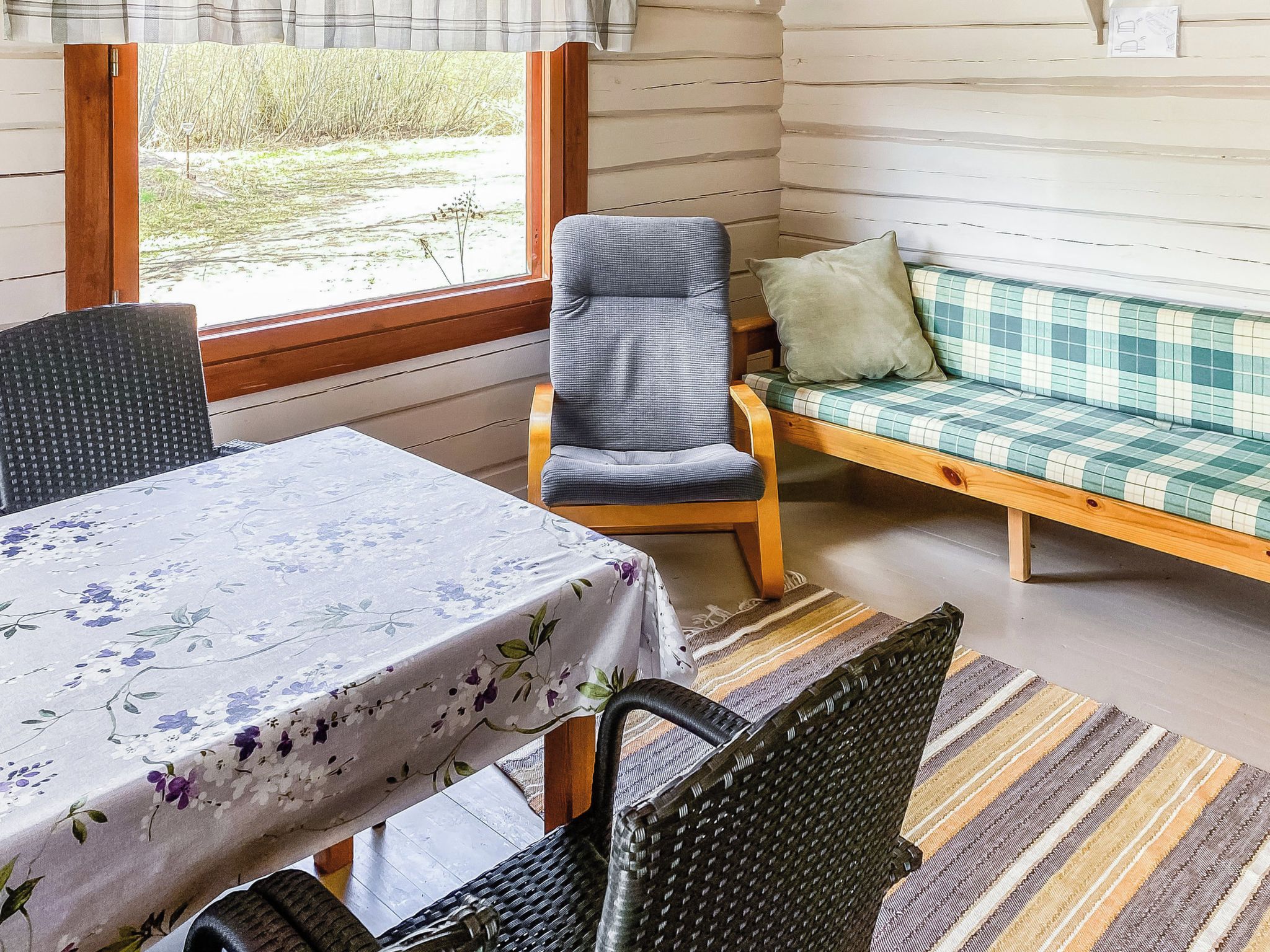 A room with a dining table, chairs, a sofa, and a window with a view of greenery.