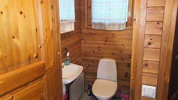A compact wooden cabin bathroom with a toilet, sink, and window.