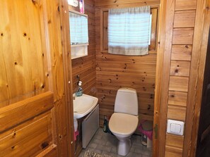 Baño de una cabaña de madera pequeña con inodoro, lavabo y ventana.
