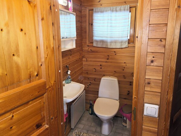 A compact wooden cabin bathroom with a toilet, sink, and window.