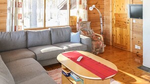 A cozy living room with a grey sofa, a wooden coffee table with a red placemat, a patterned armchair, and a television on a wooden cabinet. - Mäntyniemi by Interhome (Konnevesi)