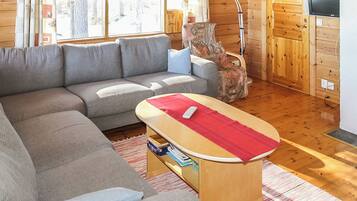 A cozy living room with a grey sectional sofa, a small wooden table with a red cloth, and a television on a wooden cabinet.