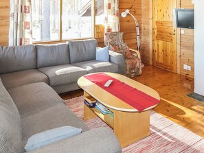 A cozy living room with a grey sectional sofa, a small wooden table with a red cloth, and a television on a wooden cabinet. - Mäntyniemi by Interhome (Konnevesi)