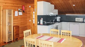 Interior em madeira com área de refeições, cozinha e um armário com copos.