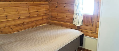 Een kleine houten kamer met een enkel bed, een raam met gordijn en een radiator.
