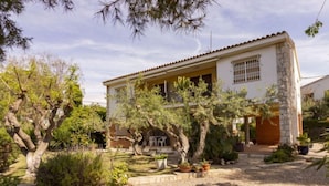 Uma casa de dois andares com fachada de pedra, telhado ladrilhado e um jardim com diversas plantas e árvores.