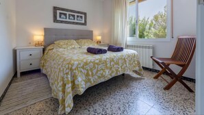 Quarto com uma cama, duas mesas de cabeceira, uma janela com cortinas, uma cadeira de madeira e um quadro na parede.