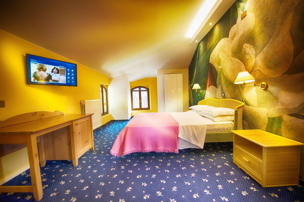 Habitación de hotel con cama, escritorio, silla, televisor y un mural en la pared.