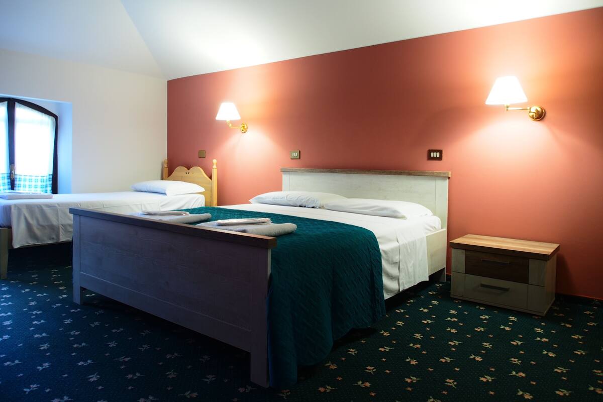 Habitación de hotel con dos camas individuales, una mesita de noche y un ventanal con vistas.