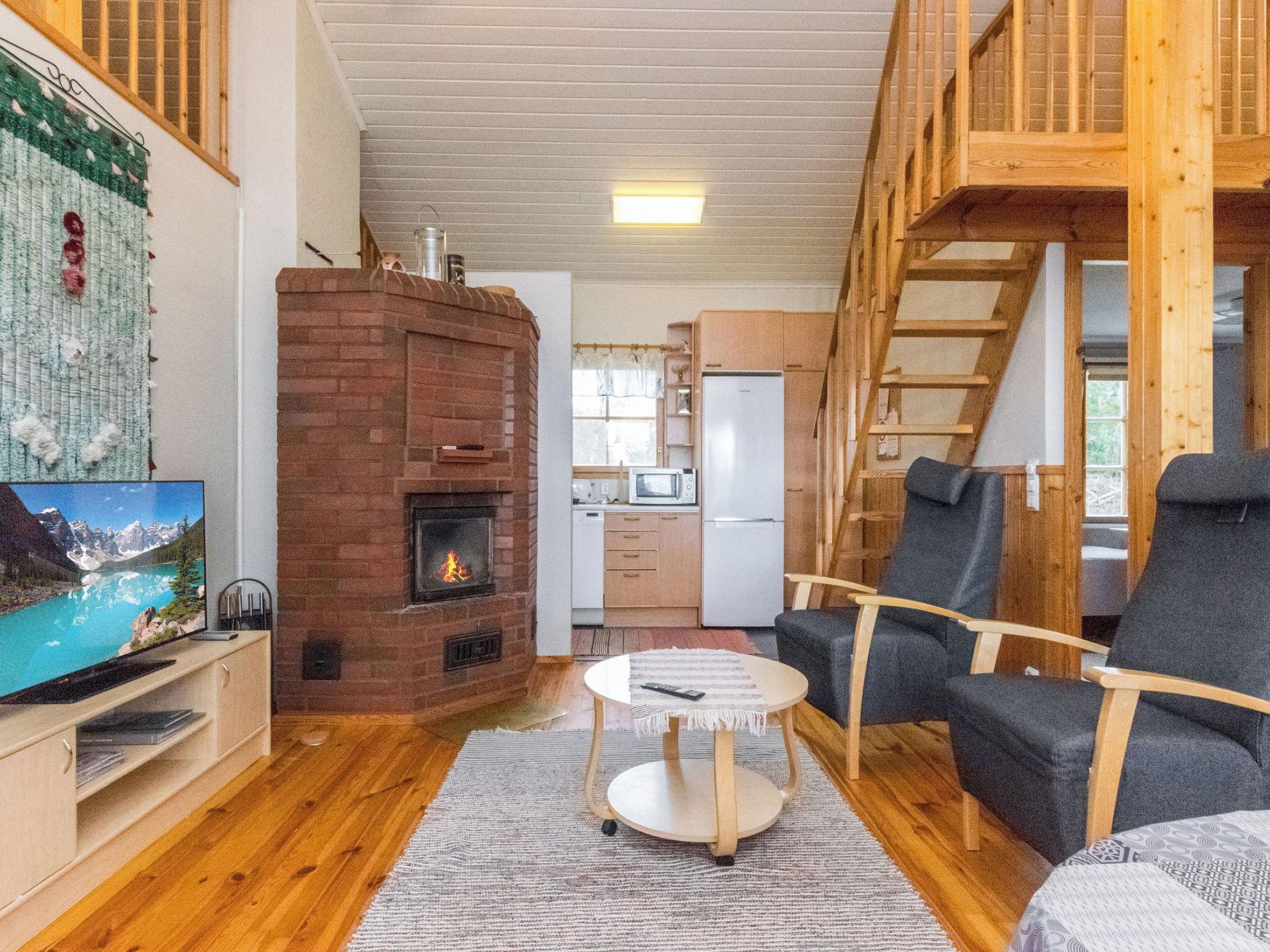 A cozy living room with a fireplace, a television, a kitchen area, and a loft space.