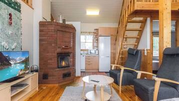 A cozy living room with a fireplace, a television, a kitchen area, and a loft space.