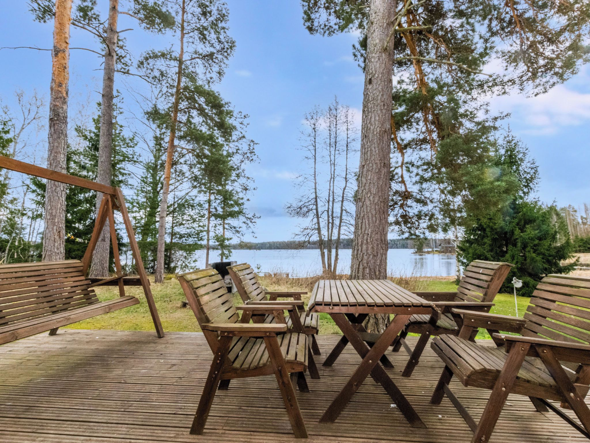 A wooden deck with outdoor seating and a swing set overlooking a lake.