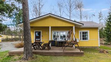 A yellow building with a porch, a table, and a swing set.