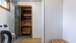 Un lavadero con lavadora, un banco, una puerta de madera que da a un armario y una ventana.