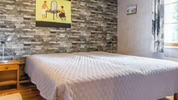 A bedroom with a bed, a nightstand, a lamp, a brick-patterned wall, and a window with curtains.