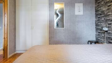 A bedroom with a large bed, a wardrobe, a mirror, and a brick wall.