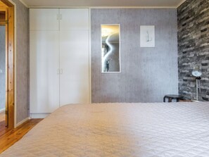 A bedroom with a large bed, a wardrobe, a mirror, and a brick wall.