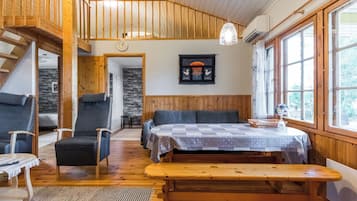 Interior acogedor de una cabaña con un banco de madera, dos sillones, una mesa y una escalera que sube a un nivel superior.