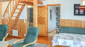 Un interior de madera con una escalera, una cama con cubrecama estampado, dos sillas verdes y una mesa de madera.